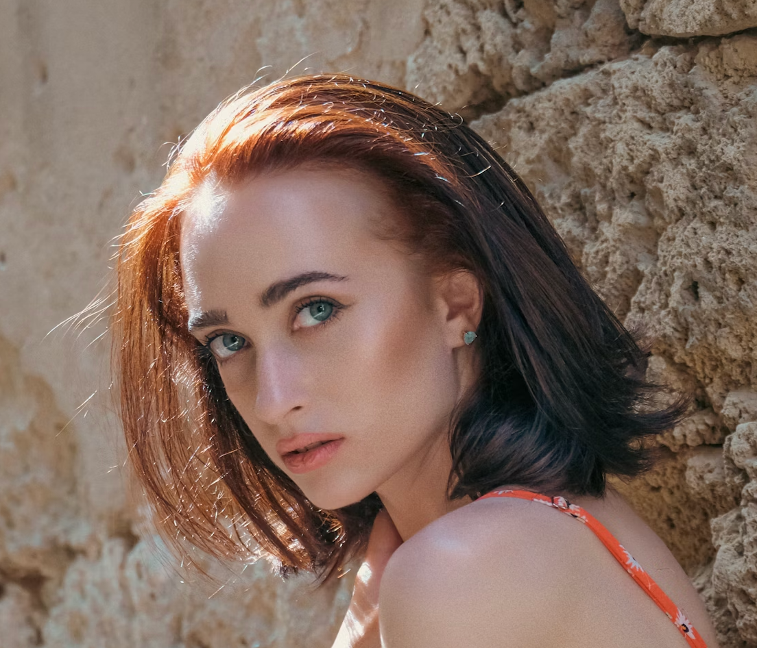 Woman with red hair posing near a stone wall